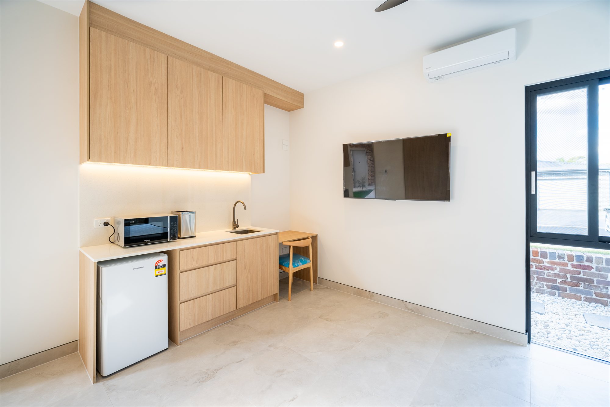 A spacious self-contained tenant room with a kitchenette, split-system air conditioning and a private courtyard entry in a completed Auzzy co-living home in Western Sydney